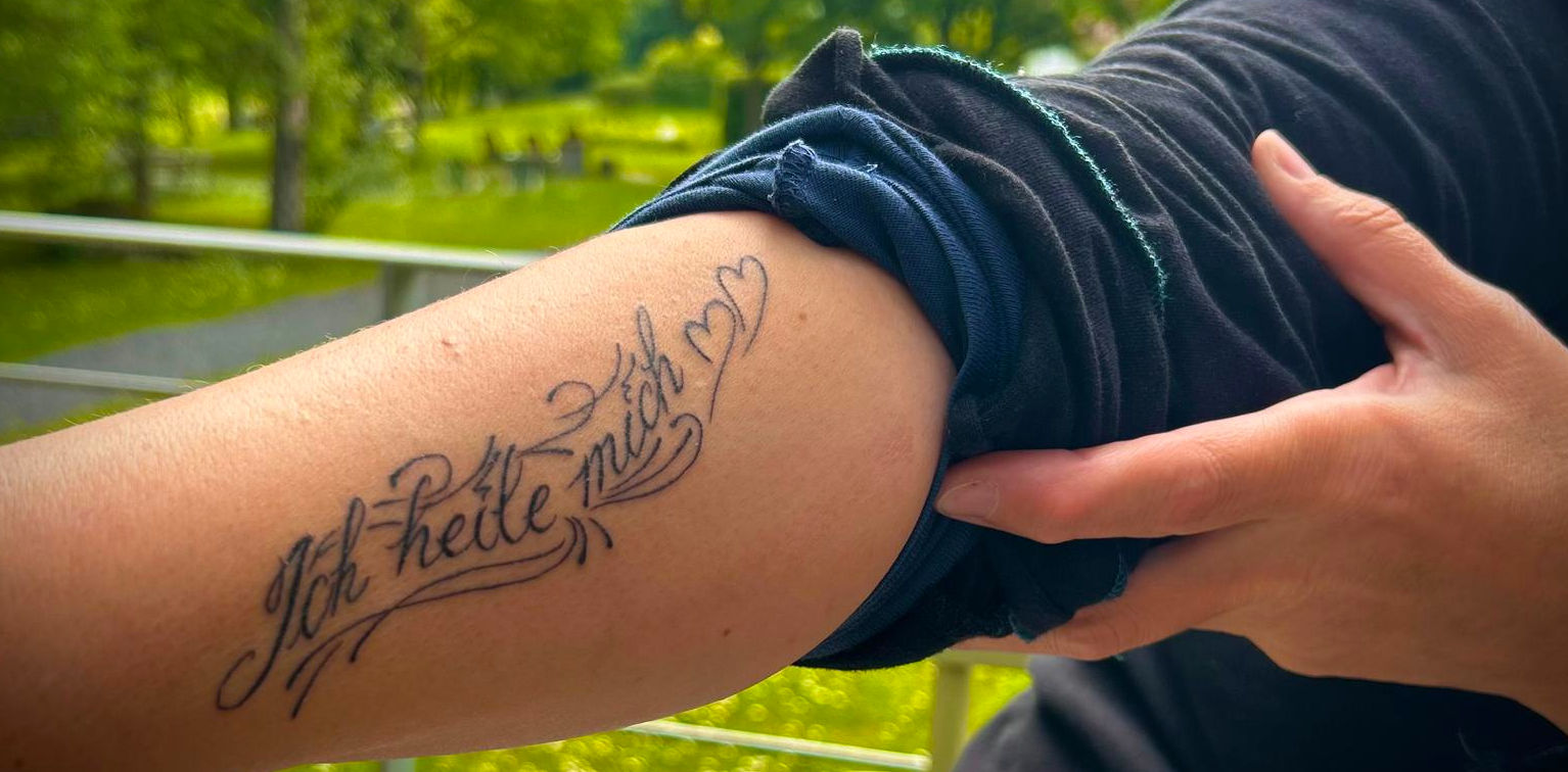 Sabine Mantel zeigt ihren rechten Unterarm, auf dem in geschwungenen Buchstaben 'Ich heile mich' steht.